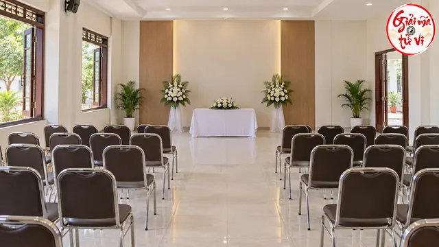 Phòng lễ trống có các hàng ghế, bàn phủ trắng và hoa bên cửa sổ