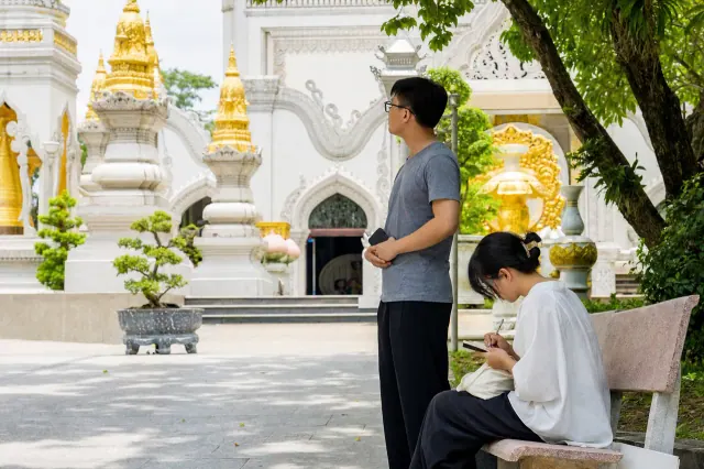 Người đàn ông quan sát công trình tháp và người phụ nữ ghi sổ dưới bóng cây