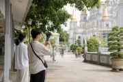 Hai người đứng ngoài sân chùa, một người cầm điện thoại chụp ảnh