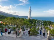 Tượng trắng quay lưng, cổng chùa, cây xanh và khách trên sân nhìn ra biển