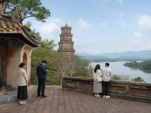 Bốn người đứng cạnh tường thấp nhìn ra sông, tháp phía sau tán cây