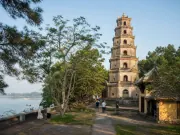 Tháp nhiều tầng bên sân có cây xanh và bốn khách, dòng sông ở phía trái