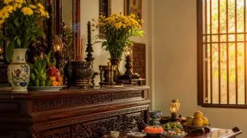 Bàn thờ gỗ có hoa vàng, quả và đồ thờ bên cửa sổ