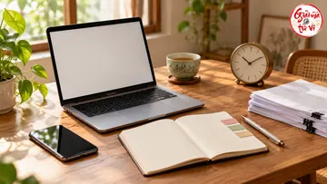 Laptop màn hình trống cạnh sổ mở, đồng hồ, điện thoại và xấp giấy trên bàn gỗ